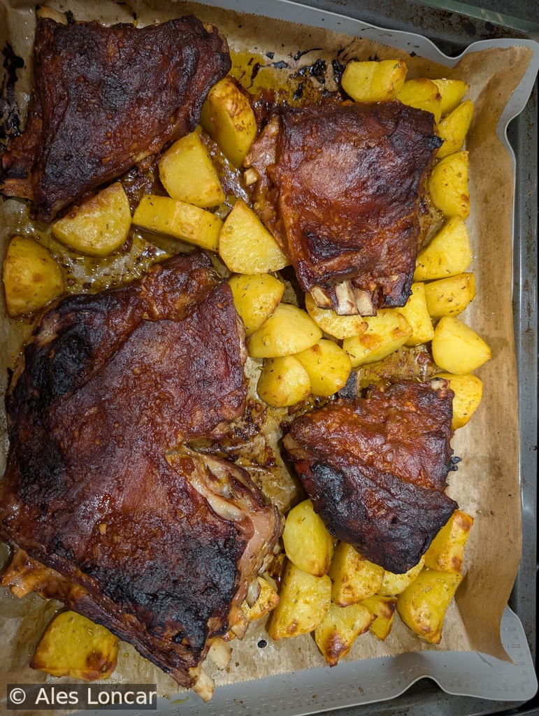 A plate of ribs coated in a glossy sweet and sour glaze, served with roasted potatoes and garnished with fresh herbs.